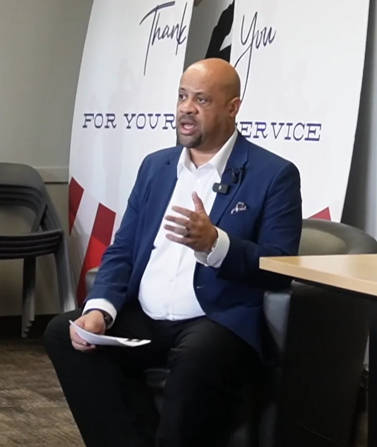Mike Roberts seated and gesturing while moderating a conversation